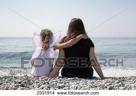 Picture - Grandmother And Granddaughter Sitting On A Pebble Beach On The Shore Of Lake Ontario; Whitby Ontario Canada. Fotosearch