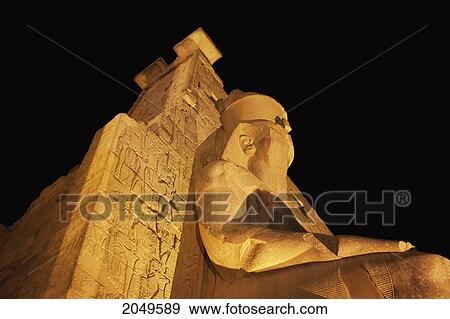 Stock Photo - Granite Colossus Of Ramses Ii On A Throne In Front Of The Entrance Pylon Of The Luxor Temple At Night, Luxor, Qina, Egypt. Fotosearch