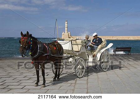 Greece, Crete, Hania, Two men sitting in horse drawn carriage, lighthouse and harbor in background. View Large Photo Image Picture - Greece, Crete, Hania, Two men sitting in horse drawn carriage, lighthouse and harbor in background.. Fotosearch