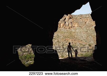 Stock Image - Greece, Crete, Woman and young girl standing in entrance to cave in wall of Zakros Gorge (or Gorge of Dead); Zakros. Fotosearch