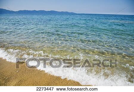Stock Photo - Greece, Halkidiki, Small waves lapping at shore on a sunny beach with crystal clear blue sea; Ierissos. Fotosearch