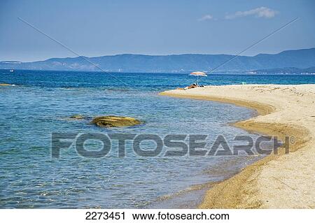 Stock Image - Greece, Halkidiki, Solitary sunbather lying under a beach parasol; Ierissos. Fotosearch