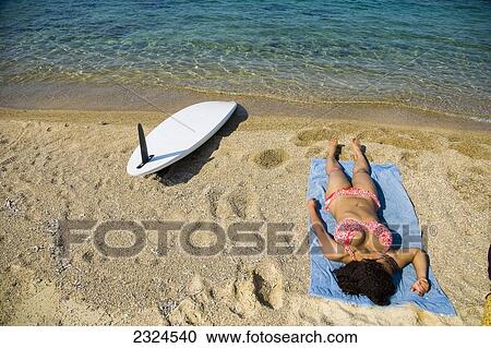 Greece, Halkidiki, Young woman sunbathing on beach with surf board on sand; Ierissos View Large Photo Image Stock Image - Greece, Halkidiki, Young woman sunbathing on beach with surf board on sand; Ierissos. Fotosearch