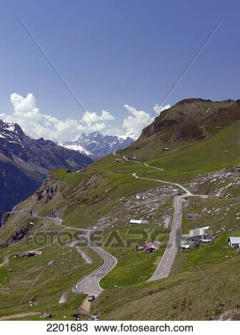 Stock Image - Green Mountainside With Scattered Buildings And Winding Road, Klausen Pass, Switzerland. Fotosearch