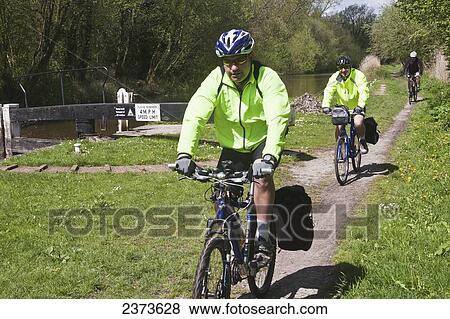 Stock Photo - Group of cyclists cycling Kennet and Avon Canal cycle path; Hungerford, Berkshire, England. Fotosearch