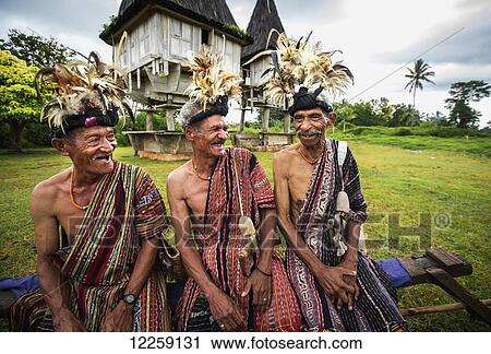 Group of men in traditional attire share a laugh with sacred houses in the background; Lospalmos district, Timor-Leste View Large Photo Image Stock Image - Group of men in traditional attire share a laugh with sacred houses in the background; Lospalmos district, Timor-Leste. Fotosearch