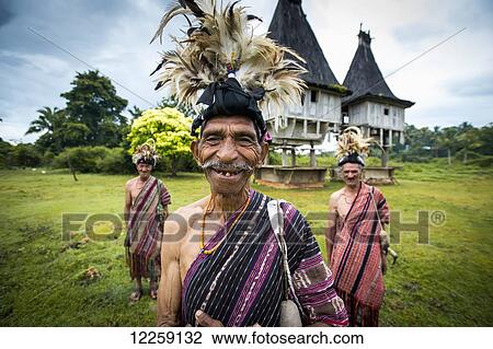 Stock Image - Group of men in traditional attire with sacred houses in the background; Lospalmos district, Timor-Leste. Fotosearch