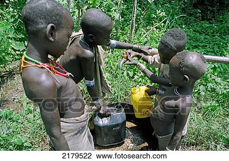 Stock Image - Group of Mursi tribal children getting water from a well dug by Christian Missionaries (Serving in Mission). Makki / South Omo / Southern Nations, Nationalities & People's Region (Ethiopia).. Fotosearch