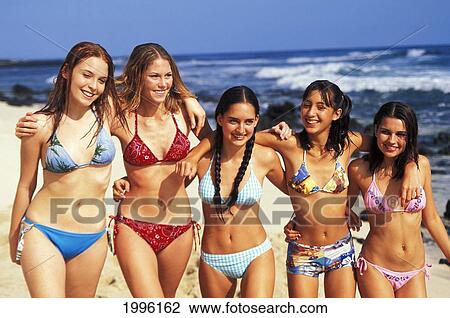 Stock Image - Group Of Teenage Girls Walking Along Beach, Arm Over Shoulders. Fotosearch