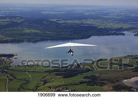 Stock Photo - Hang Glider Flying Over Fields And Lake Below; Schwangau, Germany. Fotosearch