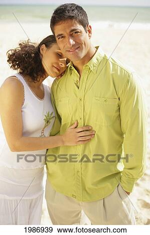 Stock Photo - Happy Couple Stand Close On Beach In Warm Afternoon Light, Woman With Eyes Closed.. Fotosearch