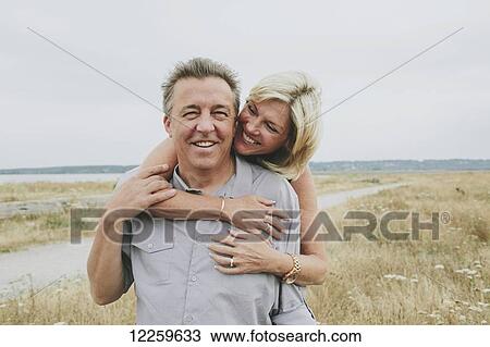 Stock Image - Happy senior couple embracing on a grassy beach; Coquitlam, British Columbia, Canada. Fotosearch