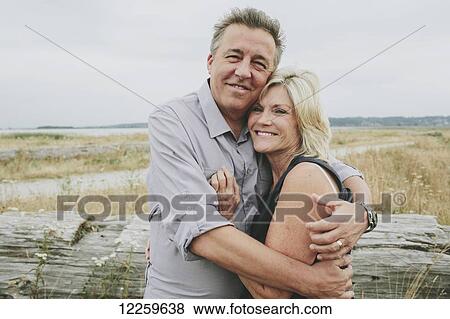 Stock Photo - Happy senior couple embracing on a grassy beach; Coquitlam, British Columbia, Canada. Fotosearch