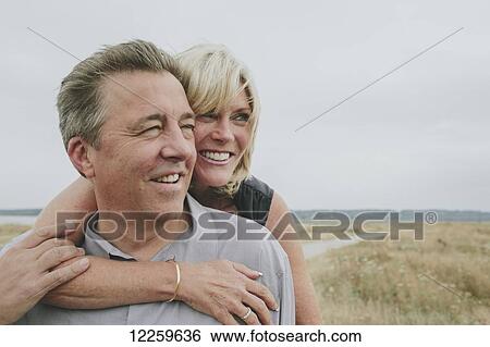 Stock Photograph - Happy senior couple embracing on a grassy beach; Coquitlam, British Columbia, Canada. Fotosearch