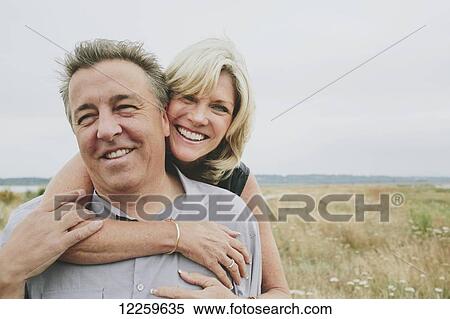 Stock Photography - Happy senior couple embracing on a grassy beach; Coquitlam, British Columbia, Canada. Fotosearch