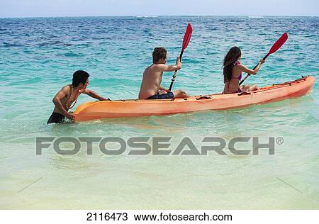 Stock Image - Hawaii, A beachboy helps a young couple begin kayaking. Fotosearch