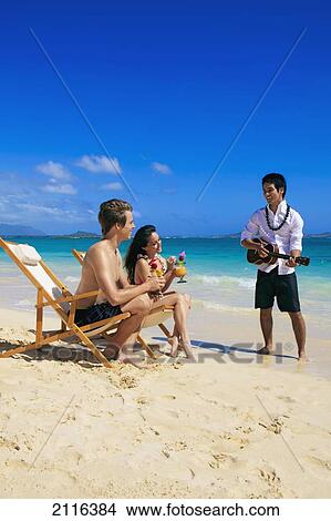 Hawaii, A man plays ukulele for a young couple on the beach. View Large Photo Image Picture - Hawaii, A man plays ukulele for a young couple on the beach.. Fotosearch