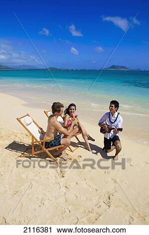 Hawaii, A man plays ukulele for a young couple on the beach. View Large Photo Image Stock Image - Hawaii, A man plays ukulele for a young couple on the beach.. Fotosearch