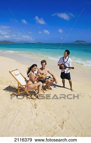 Stock Photo - Hawaii, A man plays ukulele for a young couple on the beach.. Fotosearch