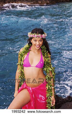 Stock Image - Hawaii, Beautiful Hawaiian Girl Wearing Bright Pink Pareo, Green Lei And Haku, Standing On Rocky Shoreline. Fotosearch