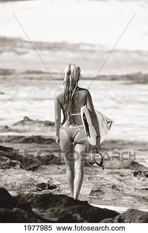 Stock Photography - Hawaii, Beautiful Young Woman Holding A Surfboard Looking Out At Ocean, View From Behind (Sepia Photograph).. Fotosearch