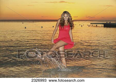 Stock Image - Hawaii, Beautiful Young Woman Playing In The Ocean At Sunset.. Fotosearch