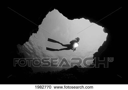Stock Image - Hawaii, Big Island, Kona, Diver With Flashlight, Framed By Cavern Entrance (Black And White Photograph).. Fotosearch