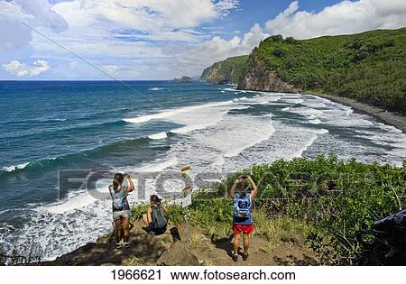 Stock Image - Hawaii, Big Island, North Kohala, Pololu Valley Trail, Women Hikers Overlooking Ocean. For Editorial Use Only.. Fotosearch