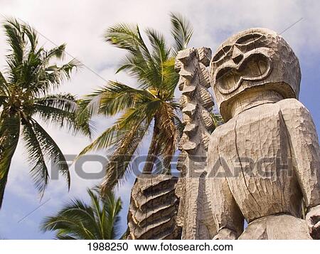 Stock Image - Hawaii, Big Island, Puuhonua O Honaunau, City Of Refuge, Ki'i Against Blue Sky And Palm Trees.. Fotosearch
