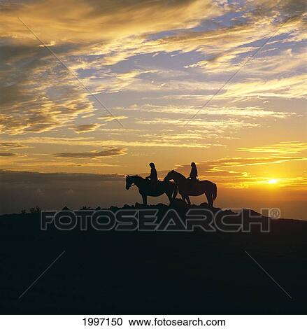 Stock Image - Hawaii, Big Island, Waialae Iki, Couple Horseback Riding At Sunset, Silhouetted A07D. Fotosearch