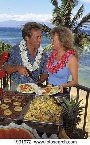 Stock Image - Hawaii, Couple At Luau Buffet, Ocean And Palm Trees In Background.. Fotosearch