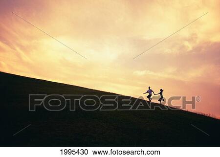 Stock Image - Hawaii, Couple Running Along A Hill At Sunset. Fotosearch