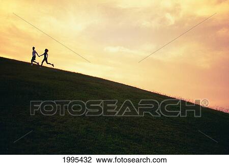 Stock Image - Hawaii, Couple Running Along A Hill At Sunset. Fotosearch