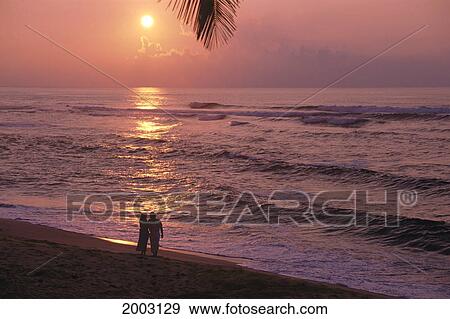 Stock Photo - Hawaii, Couple Silhouetted By Golden Orange Sunset On Beach, Standing On Shore. Fotosearch