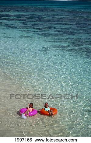 Stock Photograph - Hawaii, Distant View Of Two Local Girls On The Beach In Colorful Inner Tubes A09C. Fotosearch