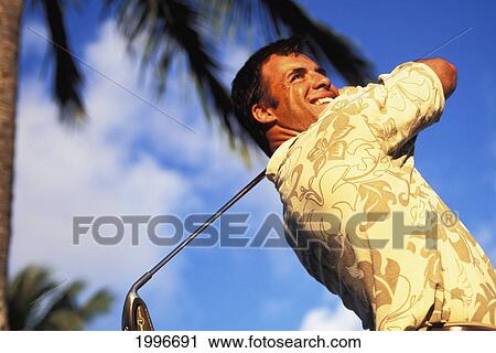 Stock Image - Hawaii, Golfer At The End Of Swing. Blue Sky And Palm Tree Blurry Background.. Fotosearch