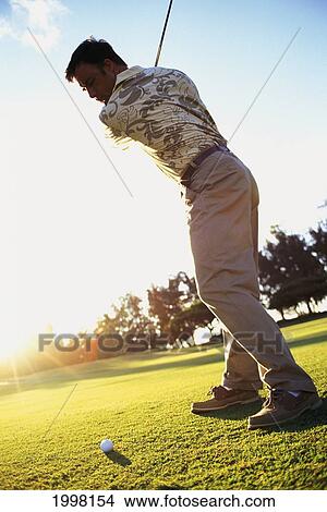 Picture - Hawaii, Golfer In Mid-Swing. Sunburst Light In Background.. Fotosearch