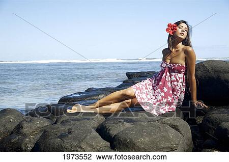 Stock Image - Hawaii, Kauai, Anini Beach, Attractive Young Woman On The Rocks With Hawaiiana Attire.. Fotosearch