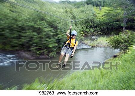Stock Image - Hawaii, Kauai, Girl On A Valley Zipline Tour Over A Stream.. Fotosearch