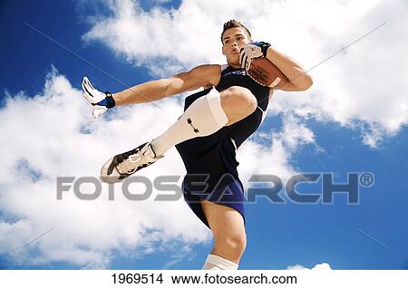 Picture - Hawaii, Kauai, Haena Beach, Fit Male Holding A Football With Beautiful Clouds In The Background.. Fotosearch