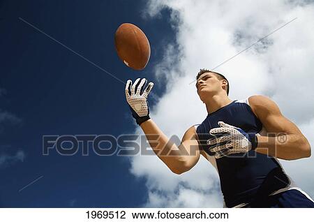 Stock Image - Hawaii, Kauai, Haena Beach, Fit Male Holding A Football With Beautiful Clouds In The Background.. Fotosearch