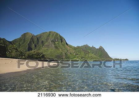 Stock Image - Hawaii, Kauai, Haena, Tunnels Beach, Clear blue water and lush green mountain peaks.. Fotosearch