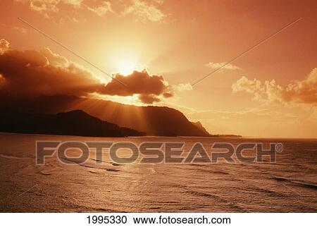 Stock Image - Hawaii, Kauai, Hanalei Bay, Bali Hai Point, Red Sunset, Sunburst From Behind Clouds. Fotosearch