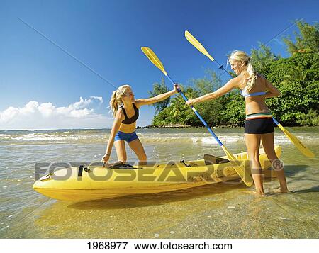 Stock Photo - Hawaii, Kauai, Hanalei Bay, Two Active Young Woman Preparing To Kayak.. Fotosearch