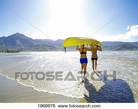 Hawaii, Kauai, Hanalei Bay, Two Active Young Woman Carrying A Kayak Into The Ocean. View Large Photo Image Stock Photograph - Hawaii, Kauai, Hanalei Bay, Two Active Young Woman Carrying A Kayak Into The Ocean.. Fotosearch