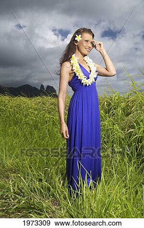Stock Photo - Hawaii, Kauai, Hanalei, Beautiful Fashion Model On A Grassy Field In A Blue Dress Wearing Plumerias.. Fotosearch