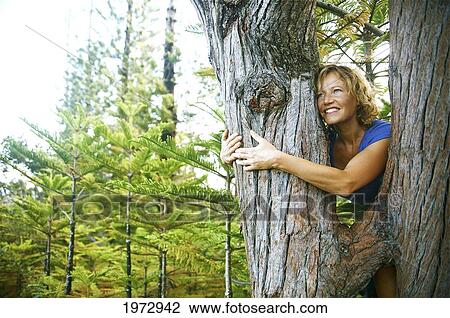 Stock Image - Hawaii, Kauai, Hanalei, Portrait Of A Beautiful Woman Hugging A Tree Trunk.. Fotosearch