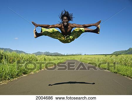 Stock Photograph - Hawaii, Kauai, Kealia, African Dancer Leaping Into The Air On Country Road.. Fotosearch