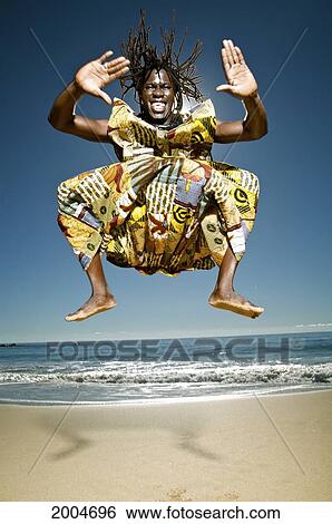 Stock Photograph - Hawaii, Kauai, Kealia Beach, African Dancer Leaping In The Air On Sandy Shore.. Fotosearch