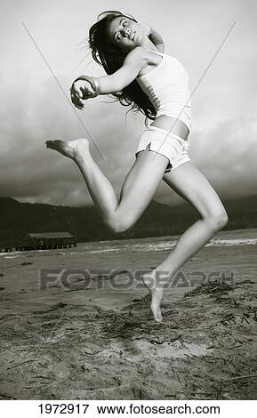 Stock Photo - Hawaii, Kauai, Kealia Beach, Attractive Young Woman On The Beach Jumping.. Fotosearch